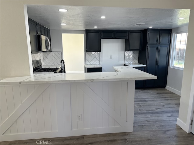 kitchen with light stone countertops, stainless steel appliances, kitchen peninsula, decorative backsplash, and light wood-type flooring