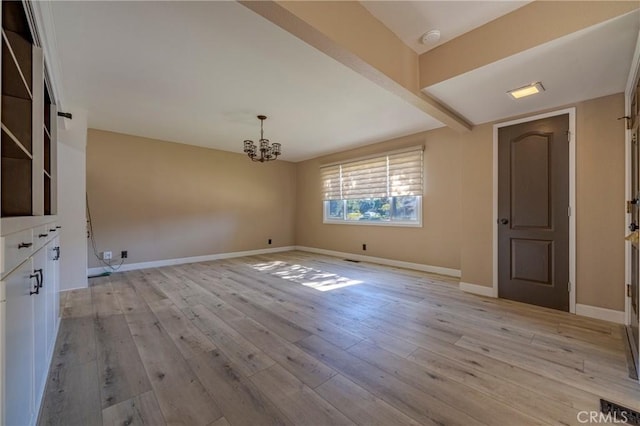 empty room featuring a notable chandelier and light hardwood / wood-style floors