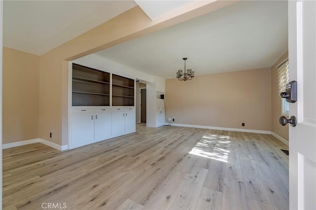 unfurnished living room with built in shelves, light wood-type flooring, and an inviting chandelier