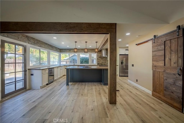 kitchen with stainless steel fridge, light wood-type flooring, a barn door, decorative light fixtures, and white cabinetry