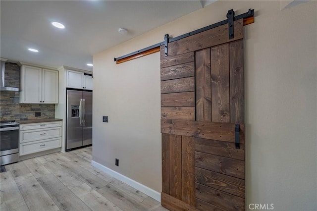 kitchen featuring a barn door, tasteful backsplash, light hardwood / wood-style floors, white cabinetry, and stainless steel appliances