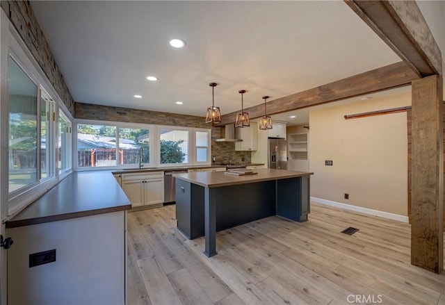 kitchen with white cabinets, wall chimney range hood, light hardwood / wood-style flooring, appliances with stainless steel finishes, and a kitchen island