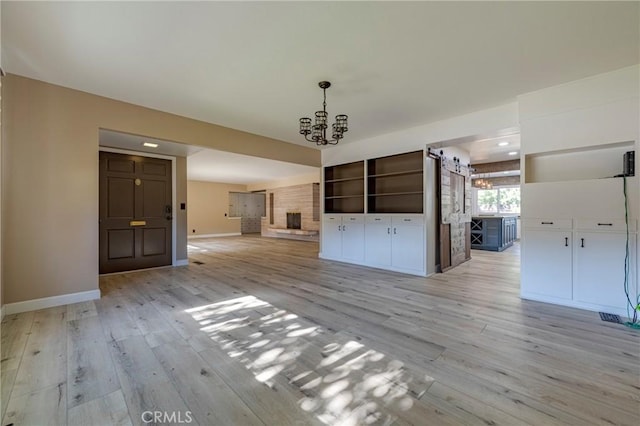 unfurnished living room with a large fireplace, light hardwood / wood-style flooring, and a notable chandelier