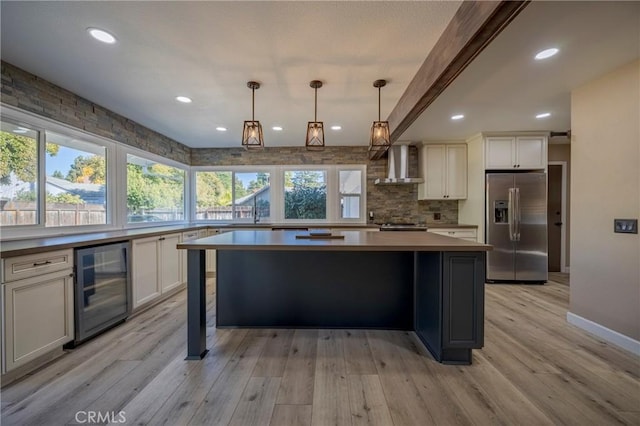 kitchen featuring stainless steel fridge, light wood-type flooring, wall chimney exhaust hood, beverage cooler, and decorative light fixtures