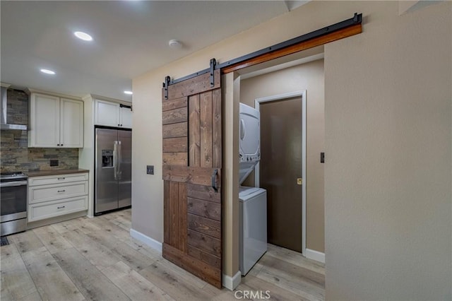 kitchen featuring stacked washer and dryer, light hardwood / wood-style flooring, a barn door, appliances with stainless steel finishes, and tasteful backsplash