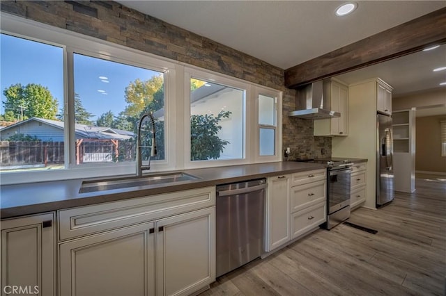 kitchen with beam ceiling, sink, stainless steel appliances, wall chimney range hood, and light hardwood / wood-style floors