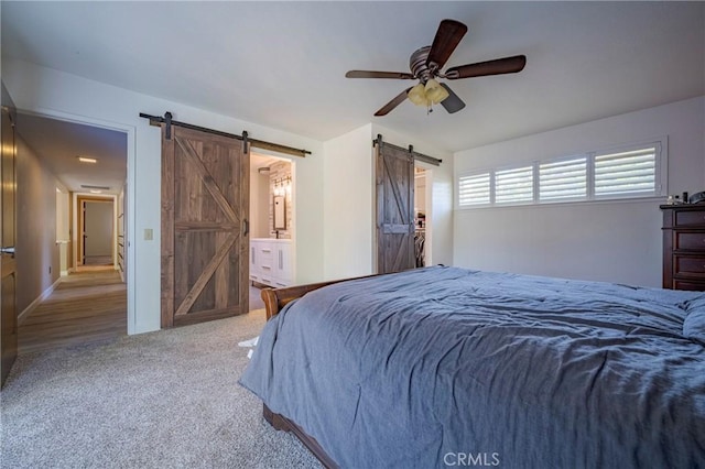 carpeted bedroom featuring a barn door, ceiling fan, and ensuite bathroom