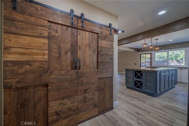 bar featuring blue cabinetry, a barn door, decorative light fixtures, and light hardwood / wood-style flooring