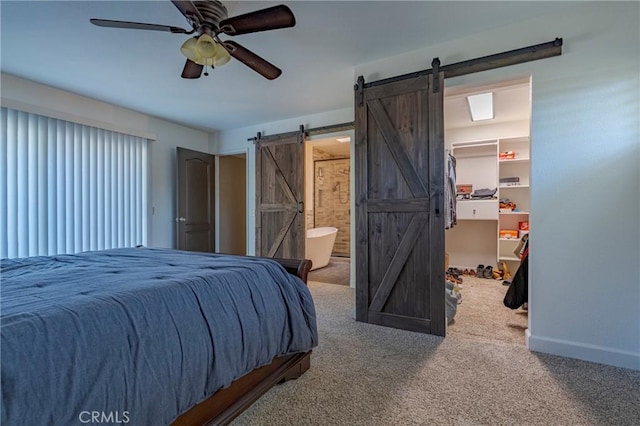 carpeted bedroom featuring ceiling fan, a barn door, a walk in closet, and ensuite bath