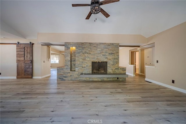 unfurnished living room featuring a barn door, ceiling fan, light hardwood / wood-style flooring, and vaulted ceiling