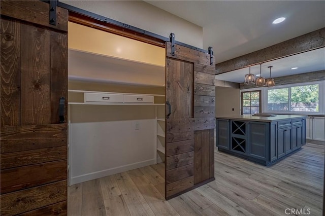 kitchen with a barn door, hanging light fixtures, light hardwood / wood-style floors, and blue cabinets