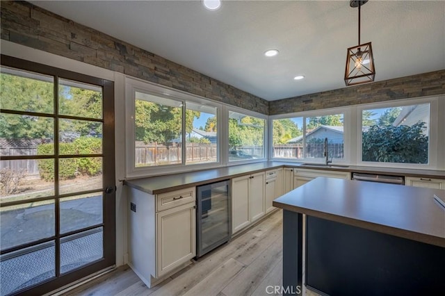 kitchen featuring white cabinetry, sink, beverage cooler, pendant lighting, and light wood-type flooring