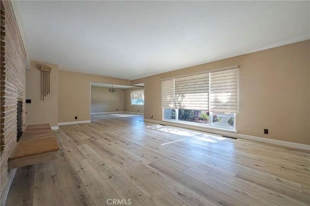 unfurnished living room with a fireplace, light wood-type flooring, and a notable chandelier