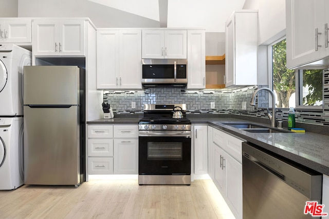 kitchen with stainless steel appliances, tasteful backsplash, white cabinets, stacked washer and clothes dryer, and sink