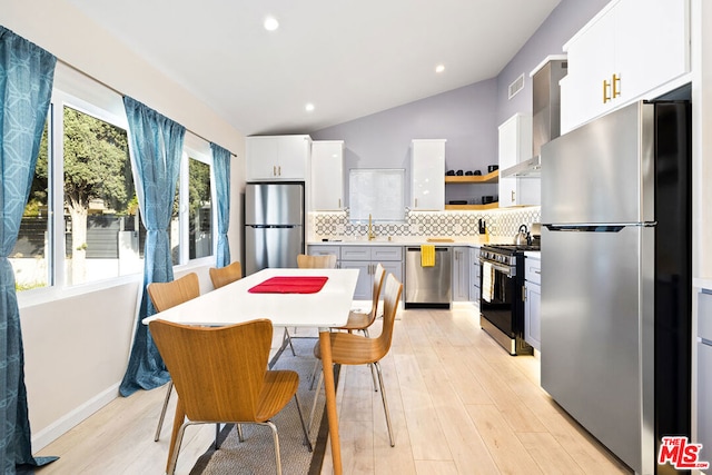 kitchen featuring stainless steel appliances, white cabinetry, wall chimney exhaust hood, lofted ceiling, and light wood-type flooring