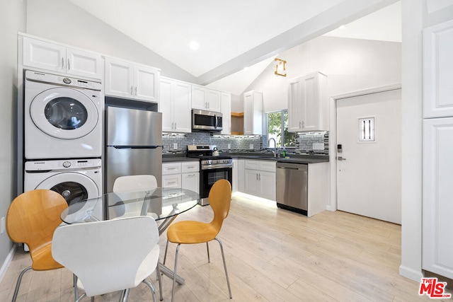 kitchen featuring vaulted ceiling, stainless steel appliances, stacked washer / dryer, white cabinetry, and sink