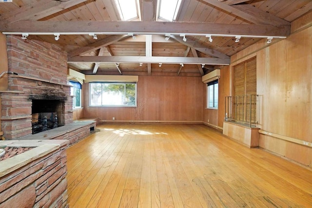 unfurnished living room with light wood-type flooring, a stone fireplace, wooden walls, and wood ceiling