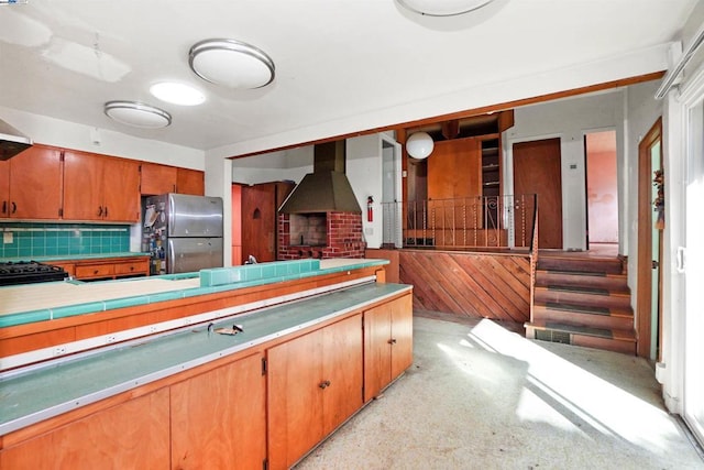 kitchen featuring black range oven, decorative backsplash, stainless steel refrigerator, and range hood