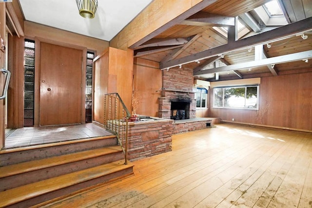 interior space with hardwood / wood-style floors, a stone fireplace, vaulted ceiling with skylight, and wooden walls