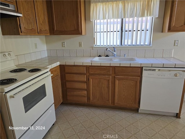 kitchen featuring tile counters, sink, white appliances, light tile patterned floors, and exhaust hood