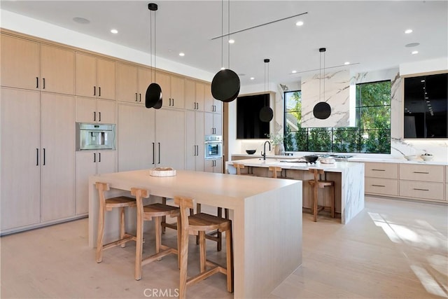 kitchen featuring a large island, light brown cabinets, oven, and hanging light fixtures