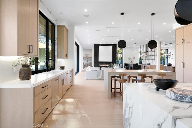 kitchen featuring light brown cabinetry, sink, a fireplace, and decorative light fixtures