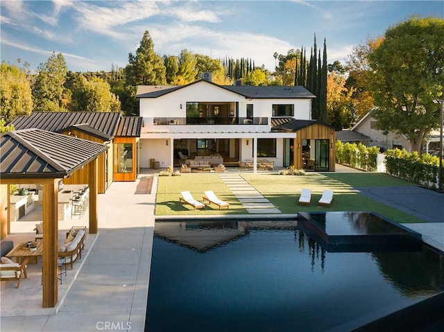 back of house with outdoor lounge area, a pool with hot tub, a patio area, and a balcony