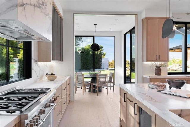 kitchen with stainless steel range, extractor fan, light brown cabinets, light hardwood / wood-style floors, and hanging light fixtures