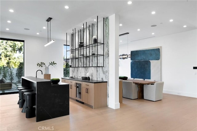 kitchen featuring a kitchen bar, pendant lighting, a center island with sink, and light hardwood / wood-style floors