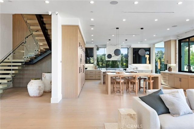 kitchen with sink, hanging light fixtures, light hardwood / wood-style flooring, a spacious island, and light brown cabinetry