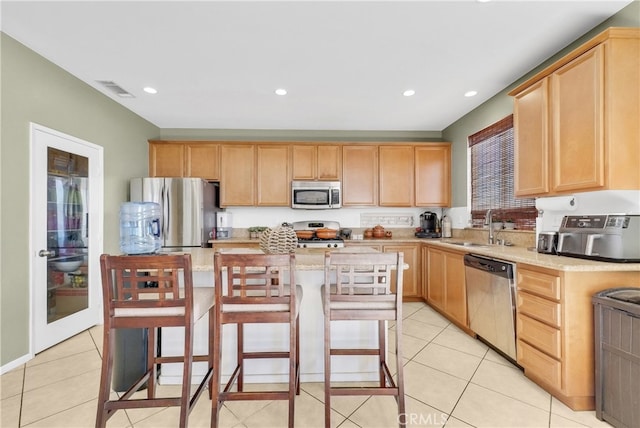 kitchen featuring a kitchen bar, stainless steel appliances, sink, light brown cabinets, and a center island