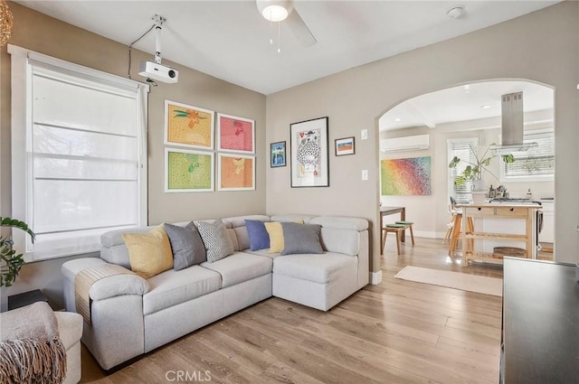 living room featuring light wood-type flooring, a wall mounted AC, and ceiling fan