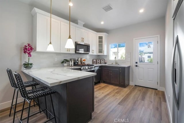 kitchen featuring white cabinetry, sink, stainless steel appliances, kitchen peninsula, and decorative light fixtures