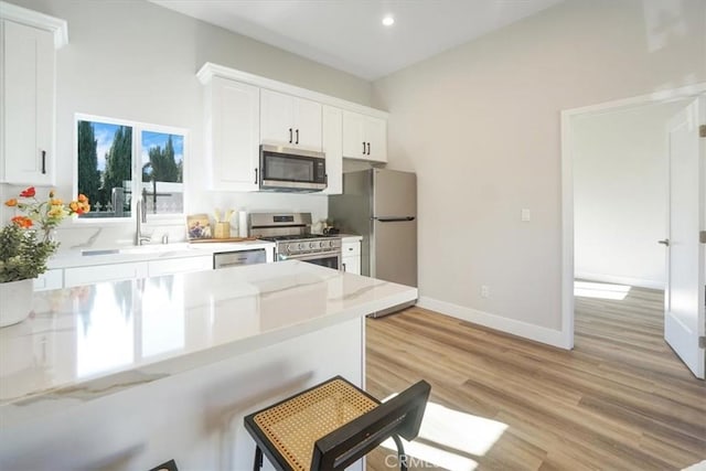 kitchen with white cabinetry, stainless steel appliances, kitchen peninsula, a breakfast bar area, and light wood-type flooring