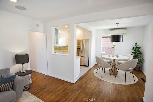 dining area featuring a wall unit AC, sink, and light wood-type flooring