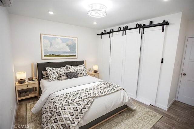 bedroom featuring a barn door, dark wood-type flooring, a wall unit AC, and a closet