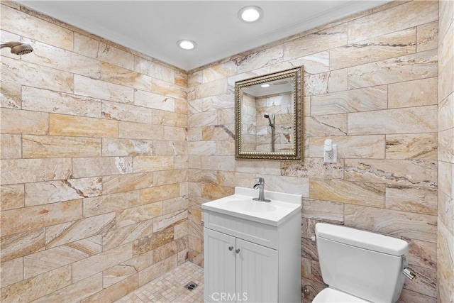 bathroom featuring vanity, crown molding, toilet, tiled shower, and tile walls