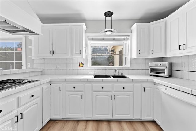 kitchen with custom exhaust hood, white dishwasher, sink, white cabinets, and tile counters