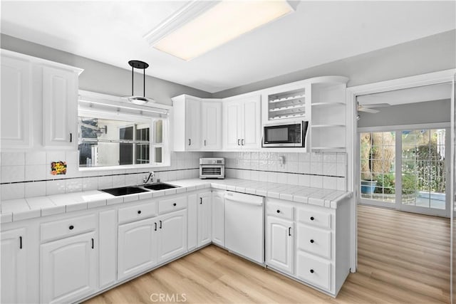 kitchen featuring white dishwasher, sink, tile counters, white cabinetry, and stainless steel microwave