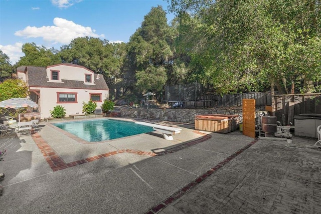 view of swimming pool featuring a hot tub, a diving board, a patio area, and a trampoline