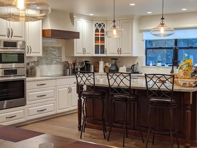 kitchen featuring black electric cooktop, a kitchen bar, custom range hood, and white cabinets