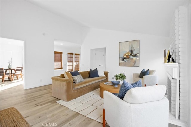 living room with a fireplace, light hardwood / wood-style floors, and high vaulted ceiling