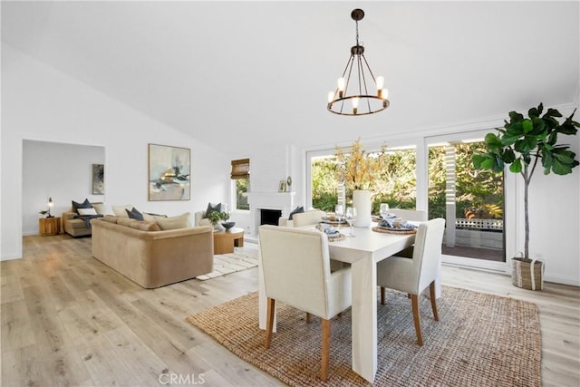 dining area featuring a chandelier, light hardwood / wood-style floors, high vaulted ceiling, and a fireplace