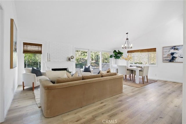 living room featuring light hardwood / wood-style flooring, high vaulted ceiling, a chandelier, and a brick fireplace