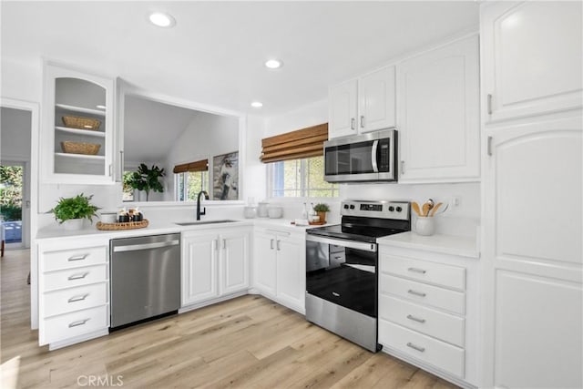 kitchen featuring appliances with stainless steel finishes, vaulted ceiling, sink, light hardwood / wood-style floors, and white cabinetry