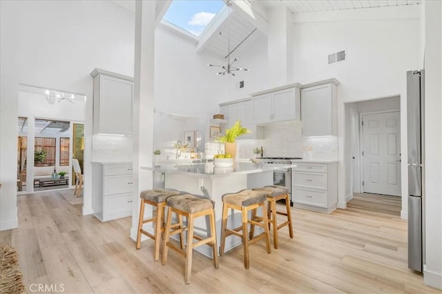 kitchen with appliances with stainless steel finishes, a kitchen bar, a skylight, tasteful backsplash, and high vaulted ceiling