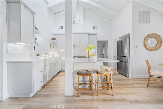 kitchen with white cabinetry, stainless steel fridge, tasteful backsplash, a breakfast bar, and beamed ceiling