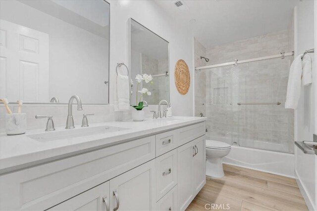 full bathroom with combined bath / shower with glass door, vanity, toilet, and hardwood / wood-style flooring