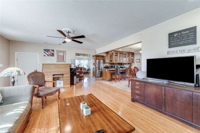 living room with light hardwood / wood-style floors, a textured ceiling, and ceiling fan