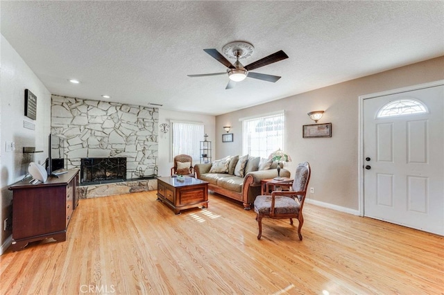 living room with ceiling fan, light wood-type flooring, and a textured ceiling